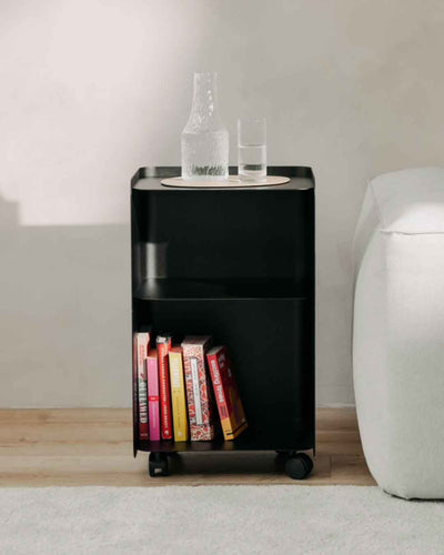 Schwarzer JUNO Rollcontainer in großer Ausführung neben einem Sofa mit Büchern und Glasflasche